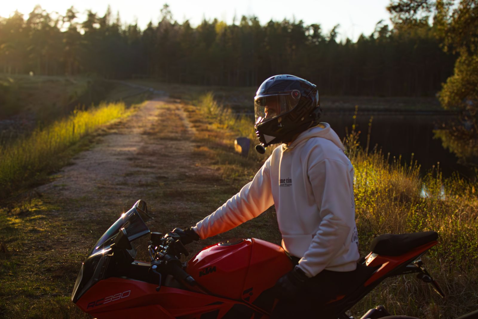 Motorcyklist på röd motorcykel vid grusväg i kvällsljus