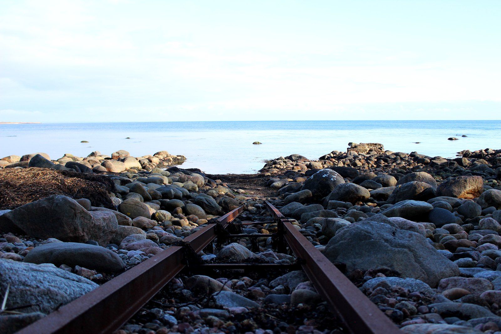 Gammal räls genom stenstrand mot havet