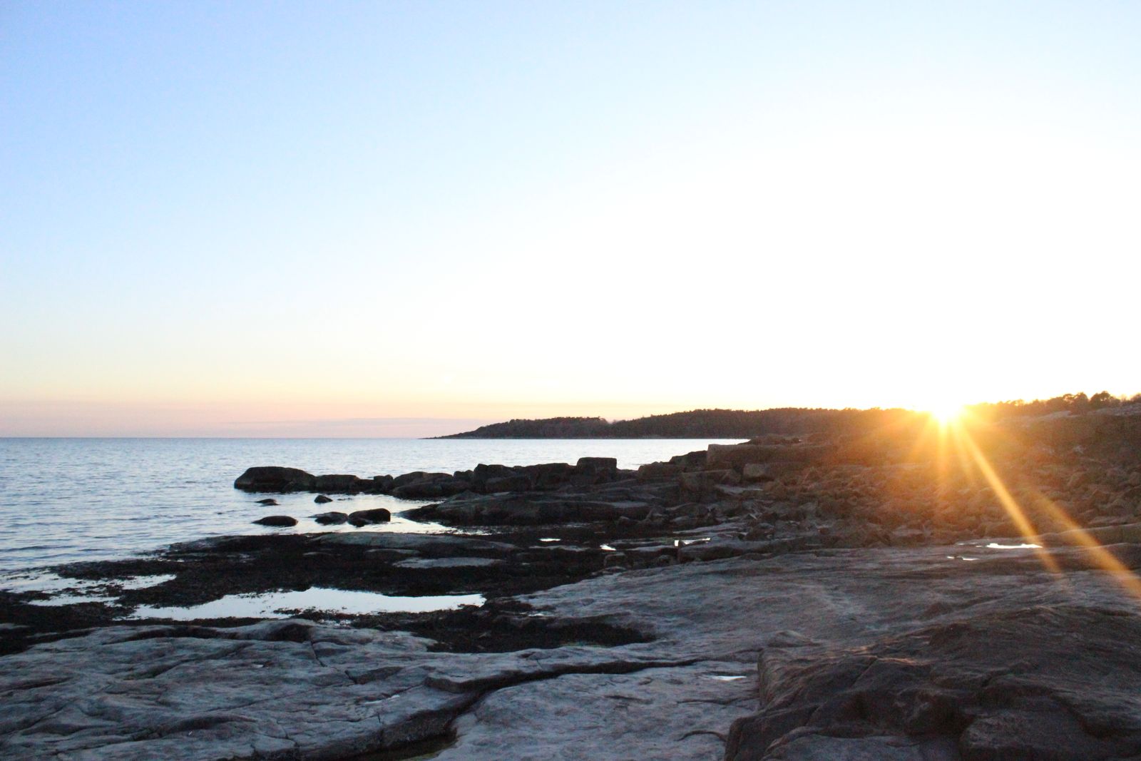 Solen sänker sig över klipphällarna vid havet